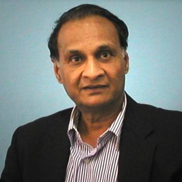 Portrait of Prof. Goverdhan Mehta, wearing a suit and red tie, smiling at the camera